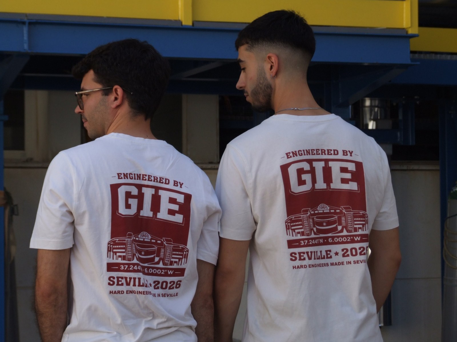 Dos socios de GEENIUS de espaldas con la camiseta &laquo;Engineered by GIE, Seville 2026&raquo;